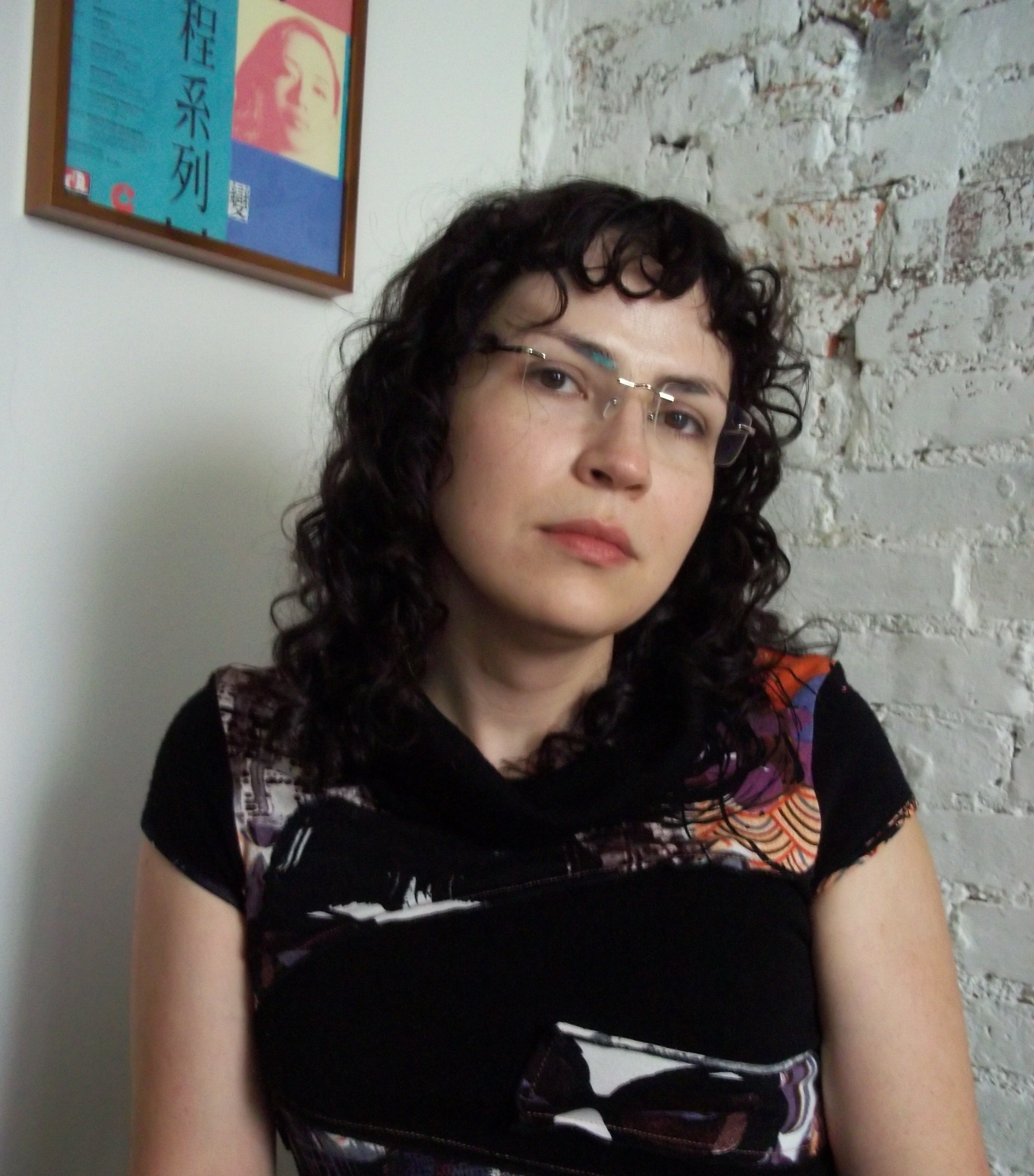 A Photo of Evie Anderson, wearing a blue knit top, standing slightly to the side of a mirror.